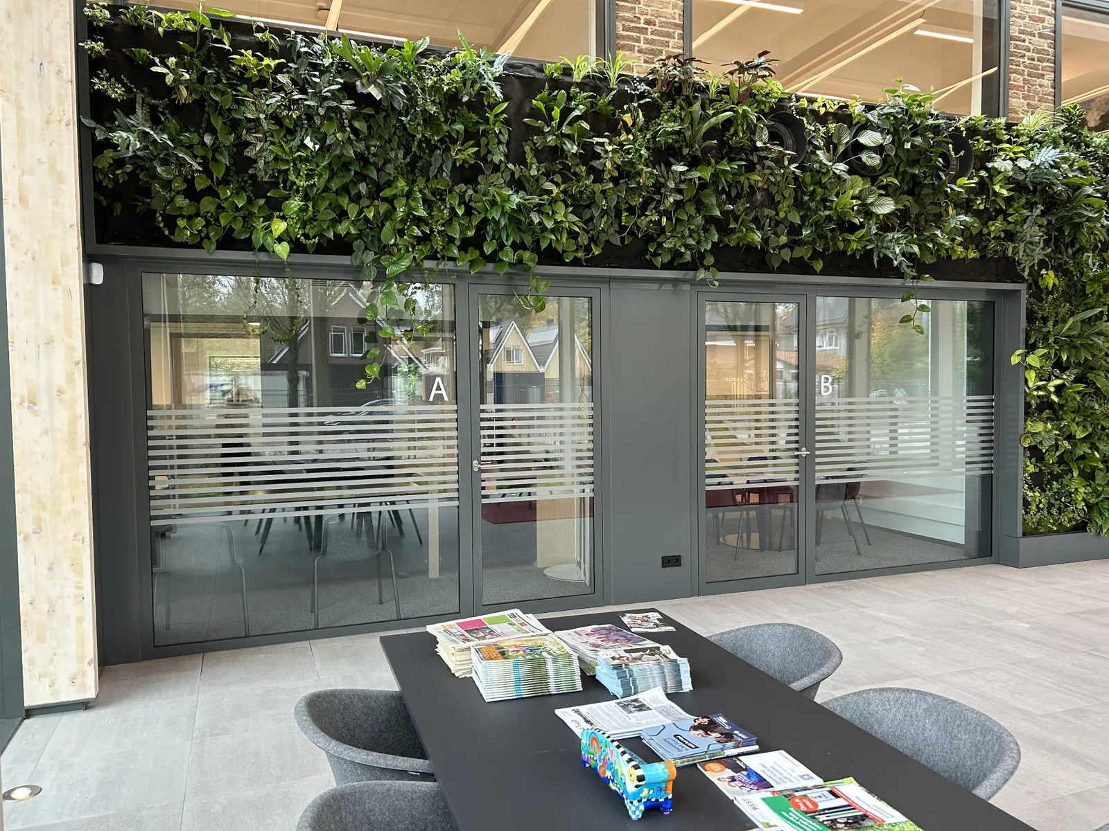 Echte kantoorruimte met groene plantwand en privacyfolie op glazen pui